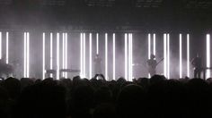 a group of people that are standing in front of some lights on a stage with guitars