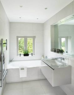 a white bathroom with a tub, sink and large mirror on the wall next to it