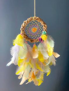 a colorful dream catcher hanging from a string on a gray background with white and yellow feathers