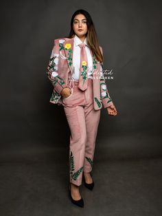 a woman in a pink suit with flowers and leaves on the side, standing against a gray background