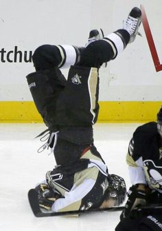 a hockey player falls on the ice while another plays in the background with his arms outstretched