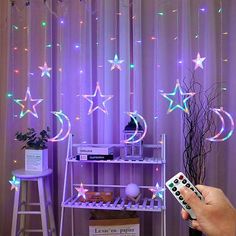 a person holding a remote control in front of a purple curtain with stars and moon lights