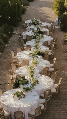 a long table is set up with white linens and greenery for an outdoor wedding reception