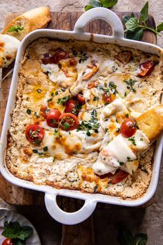 a casserole dish with tomatoes, cheese and bread