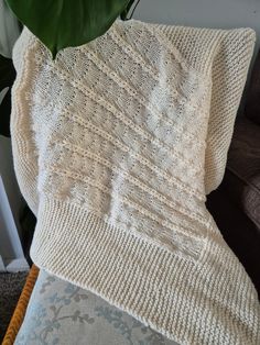 a white knitted blanket sitting on top of a couch next to a green plant