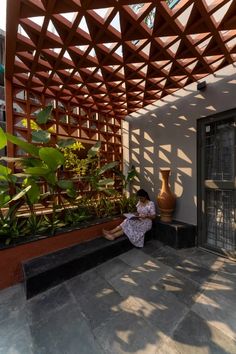 a woman sitting on the ground in front of a building with a wooden pergolated roof