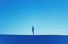 a person standing on top of a hill under a blue sky with the moon in the distance