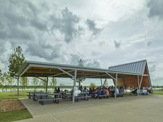 a group of people sitting at picnic tables under a covered area in the middle of a field