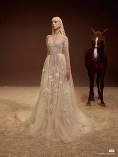 a woman standing next to a horse wearing a wedding dress with long sleeves and flowers on it