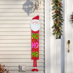 a santa clause door hanger on the side of a house with christmas decorations around it