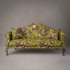 a green couch with pink and blue flowers on it's back, against a gray background