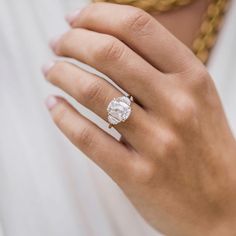 a woman's hand with a diamond ring on her left hand, wearing a white shirt