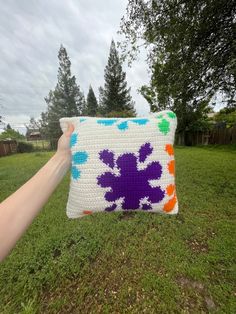 a hand holding a colorful pillow in the grass