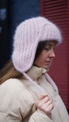 a woman wearing a pink hat while standing in front of a red building with her eyes closed