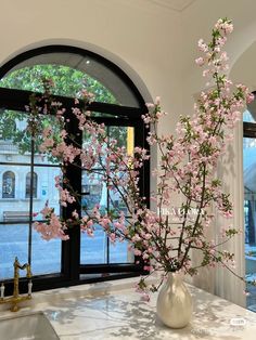 a vase filled with pink flowers sitting on top of a counter next to a window