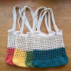 three crocheted shopping bags sitting on top of a wooden table next to each other