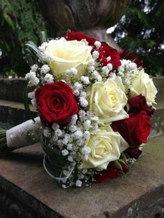 a bouquet of red and white roses sitting on top of a stone slab in front of a fountain