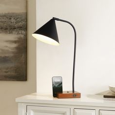 a black lamp sitting on top of a white dresser next to a phone and remote control