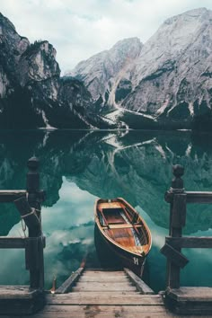 a small boat sitting on top of a lake next to a wooden dock with mountains in the background