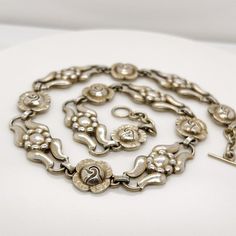 A very fine Georg Jensen necklace in sterling silver.  Model No. 10.  With alternating rose and stylized floral links, traces of its original gilding, and a toggle clasp.  Designed by Georg Jensen and bearing an old GI mark.  At approximately 14 1/2 in., the necklace is a snugly fitting, true choker.  Simply a great piece!  Date: 20th Century  Overall Condition: It is in overall good, as-pictured, used estate condition.  Condition Details: The links appear to retain some of an original gilding o Vintage White Gold Metal Necklace, Victorian Hallmarked Link Necklace, Victorian Link Necklace Hallmarked, Silver Link Necklace With 17 Jewels, Vintage White Gold Necklace With Sterling Silver Clasp, Vintage White Gold Necklaces With Sterling Silver Clasp, Vintage Link Jewelry For Anniversary, Vintage Sterling Silver Link Jewelry, Antique Silver Link Necklace