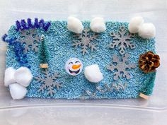 a close up of a snowman on a piece of cloth with cotton balls and pine cones