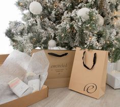 a christmas tree with white ornaments and presents in brown paper bags on the floor next to it