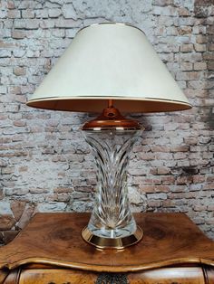 a glass lamp sitting on top of a wooden table next to a brick wall in a room