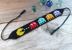 a cross - stitch pacman lanyard on a wooden table next to some glass beads