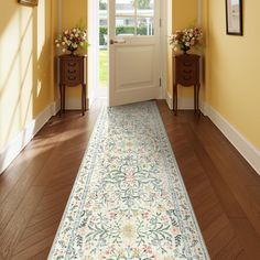 a hallway with yellow walls and wooden floors has a floral rug on the floor next to an open door