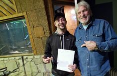 two men standing next to each other in front of a fish tank holding a piece of paper