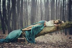 a woman laying on top of a tree branch in the woods