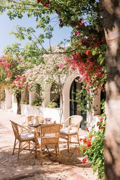 an outdoor dining area with wicker chairs and table surrounded by flowers on the outside wall