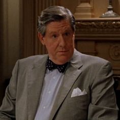 an older man in a suit and bow tie looking at the camera while sitting down