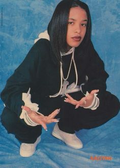 a woman with long black hair sitting on a blue background holding her hands out to the side