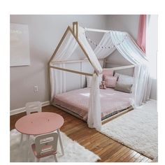 a white canopy bed sitting in a bedroom next to a pink table and small chair