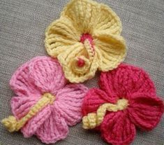 three crocheted flowers sitting on top of a gray cloth covered floor next to each other