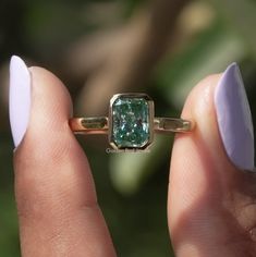 a close up of a person holding a ring with a green diamond in it's middle