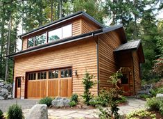 a large wooden house in the woods with lots of trees around it and rocks on the ground