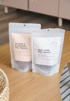 two bags of dog treats sitting on top of a wooden table next to a wicker basket