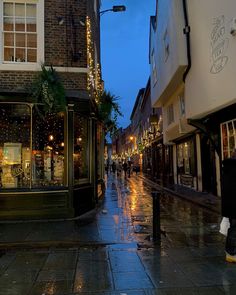 a wet street with people walking down it at night, and lights on buildings in the background