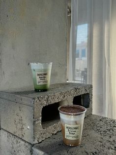 two cups of coffee sitting on top of a stone counter next to a window sill