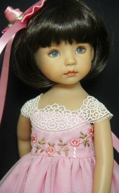 the doll is wearing a pink dress with flowers on it's chest and hair tied back