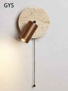 a wooden clock on the wall next to a light fixture with a cord hanging from it