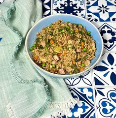 a bowl filled with rice and vegetables on top of a blue and white tile floor