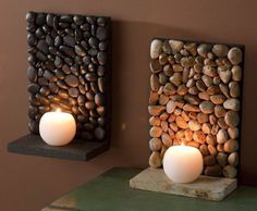 two lit candles sitting on top of a table next to rocks and stones wall art