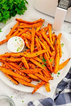 baked sweet potato fries on a white plate with parsley in the background and an air fryer to the side