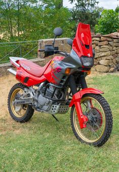 a red motorcycle parked on top of a lush green field next to a stone wall