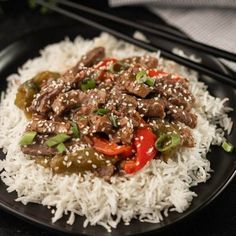 a black plate topped with white rice and stir fry beef on top of green peppers