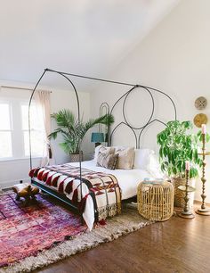 a bed room with a neatly made bed next to a large rug and potted plants