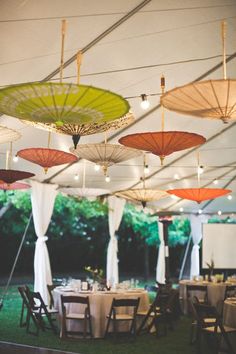 several umbrellas are hanging from the ceiling in an outdoor tent with tables and chairs